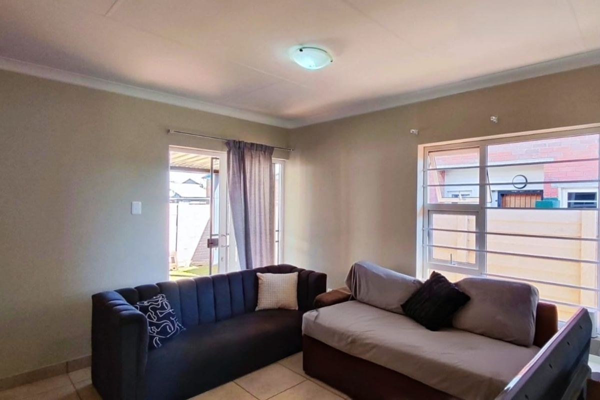 A functional living room featuring tiled flooring, large windows with security bars, and a sliding door providing access to the exterior.