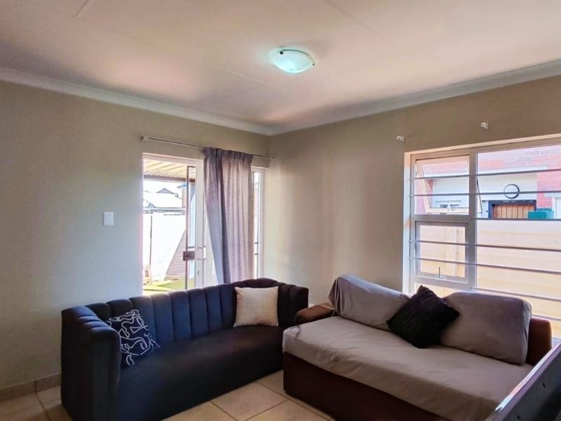 A functional living room featuring tiled flooring, large windows with security bars, and a sliding door providing access to the exterior.