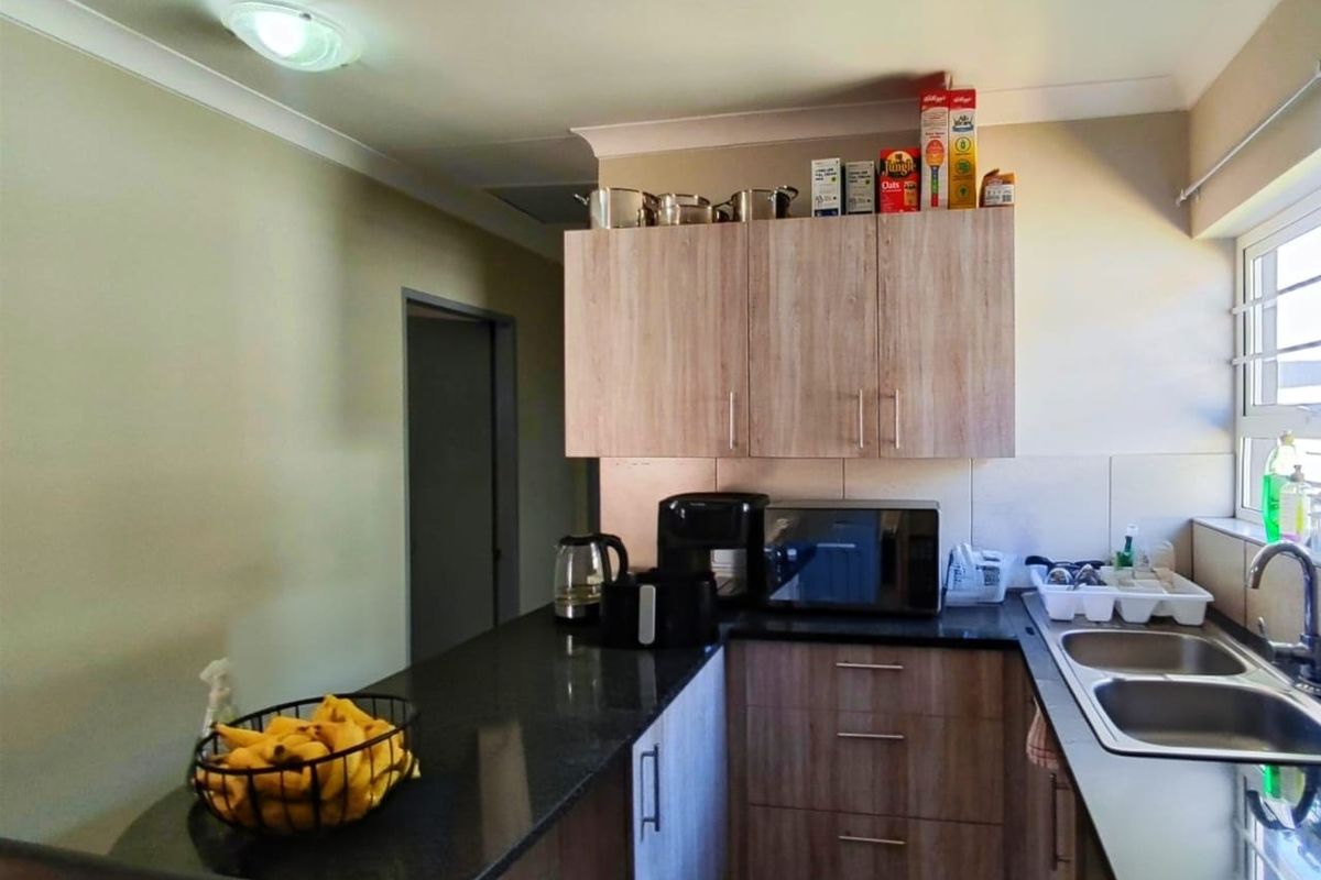 A functional kitchen featuring wood-look laminate cabinetry, dark granite countertops, and a double stainless steel sink with a tiled splashback.