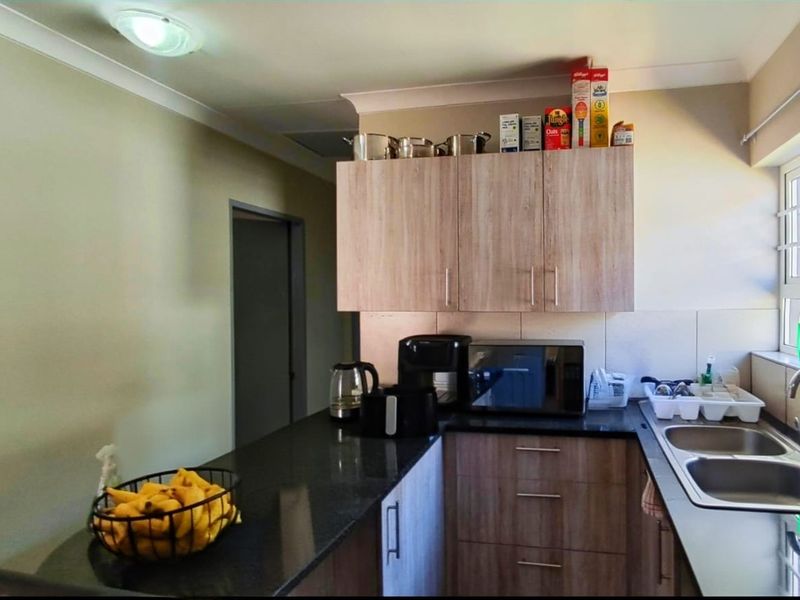 A functional kitchen featuring wood-look laminate cabinetry, dark granite countertops, and a double stainless steel sink with a tiled splashback.