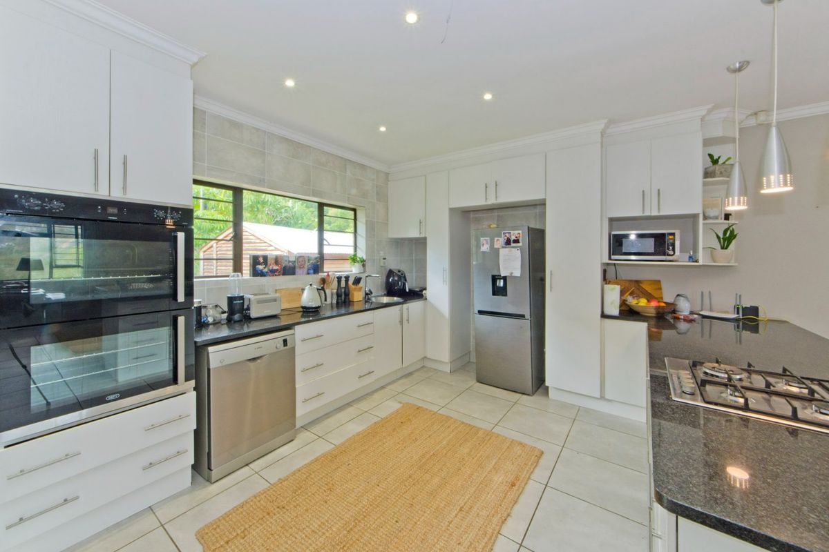 Modern kitchen featuring white cabinetry, granite countertops, a gas hob, built-in oven, and tiled flooring with ample storage space.