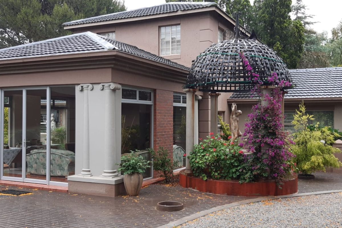 Rear exterior view featuring a paved patio, decorative metal gazebo, and a modern extension with large aluminium sliding doors and classic column detailing.