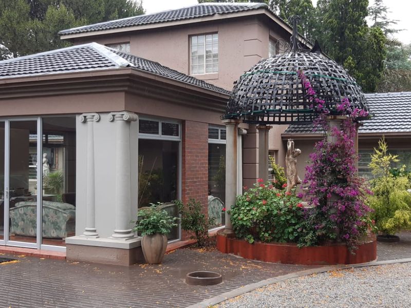 Rear exterior view featuring a paved patio, decorative metal gazebo, and a modern extension with large aluminium sliding doors and classic column detailing.