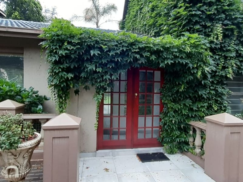 A rear patio area featuring tiled flooring, a balustrade, and red-framed French doors, partially covered by established climbing ivy.