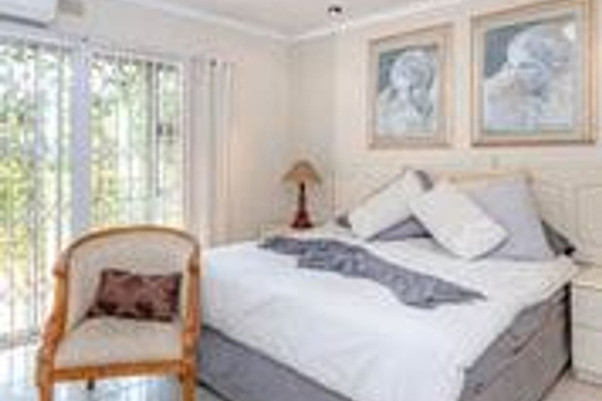 A well-lit bedroom featuring tiled flooring, recessed downlights, and a sliding glass door with security gate providing access to the exterior.