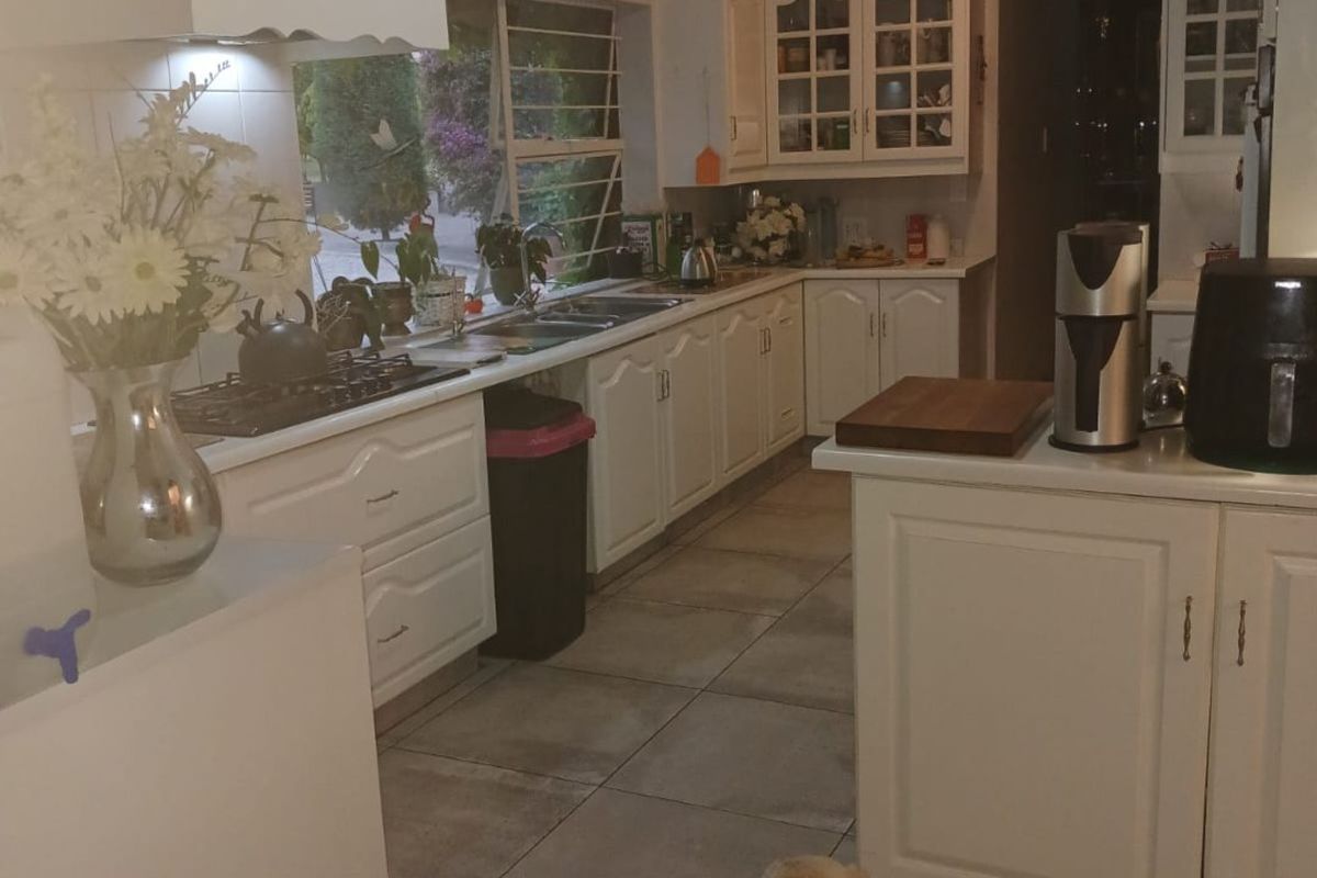 A functional kitchen featuring white cabinetry, tiled flooring, a gas hob with extractor fan, and a double sink under a window.