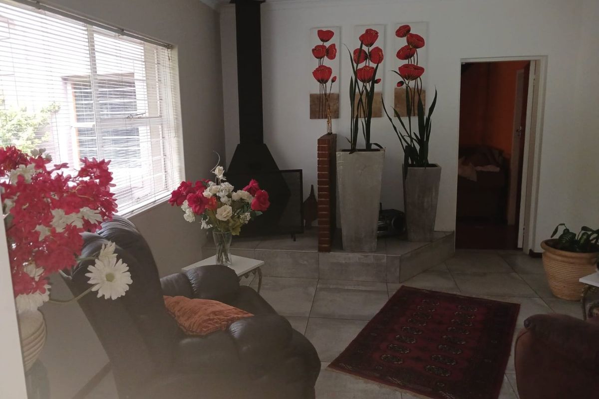 A living room featuring tiled flooring, a freestanding fireplace, and large windows with venetian blinds.