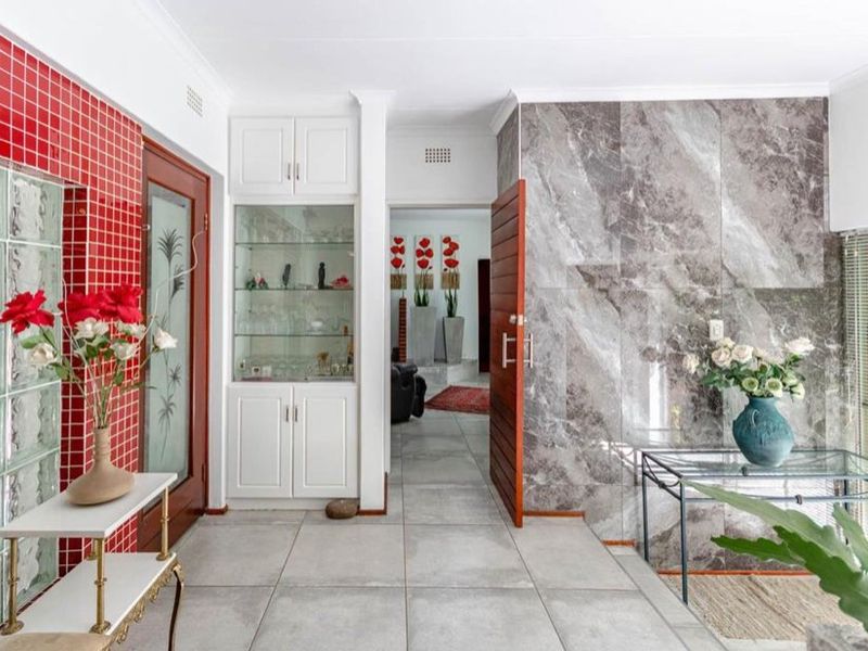 A bright entrance hall featuring tiled flooring, a striking red tiled feature wall, glass block accents, and elegant marble-effect wall cladding.