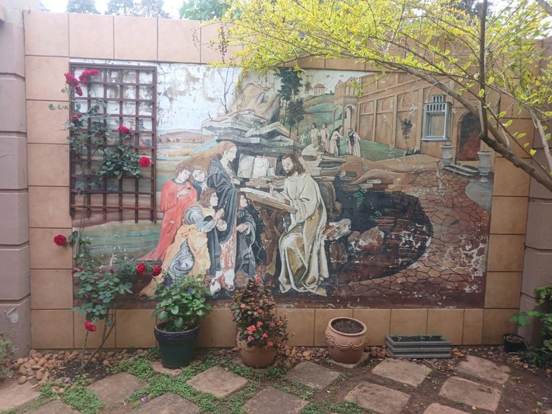 A garden area featuring a large decorative mural on a tiled wall, complemented by stone paving and a wooden trellis.