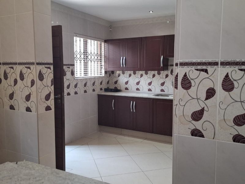 A clean, functional kitchen featuring dark wood cabinetry, tiled splashbacks, and neutral floor tiles, viewed from an adjacent space.