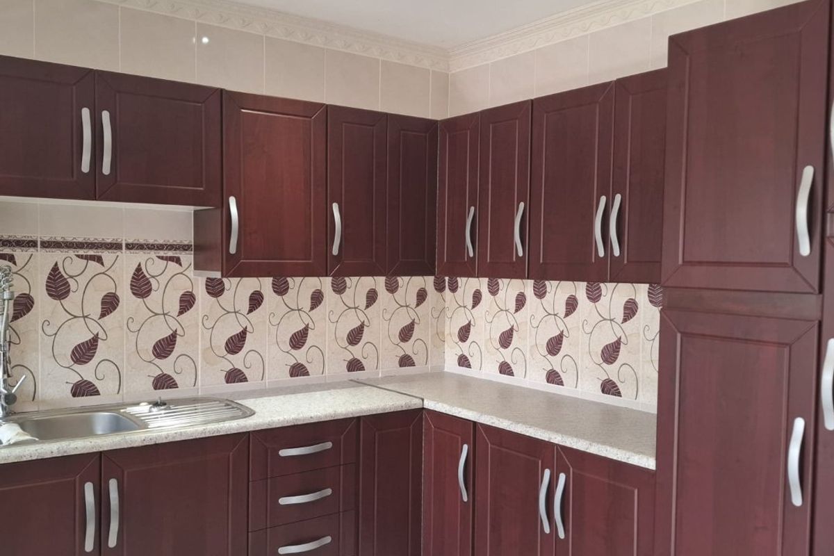A functional kitchen featuring dark wood cabinetry, laminate countertops, a stainless steel sink, and a decorative tiled backsplash.