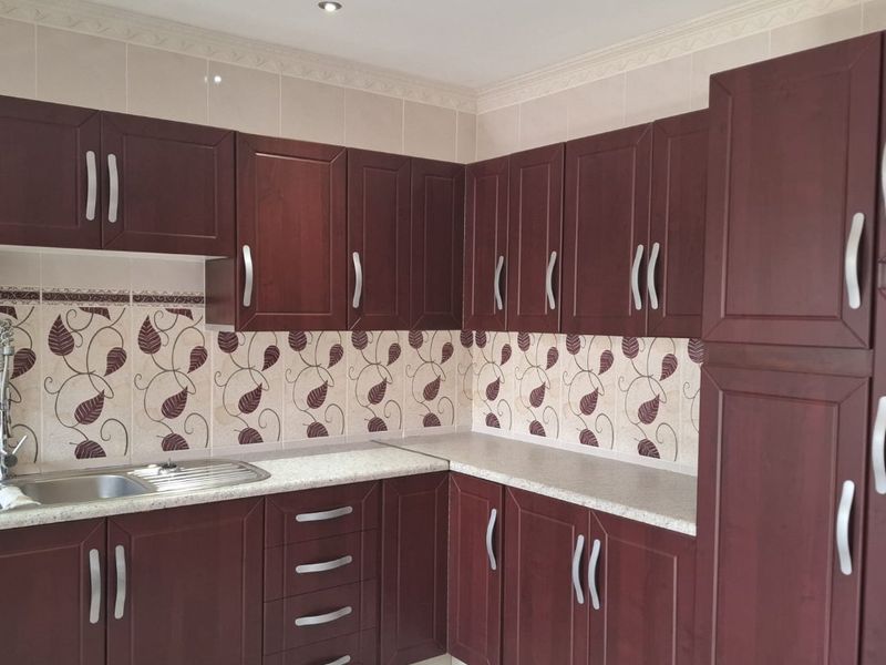 A functional kitchen featuring dark wood cabinetry, laminate countertops, a stainless steel sink, and a decorative tiled backsplash.