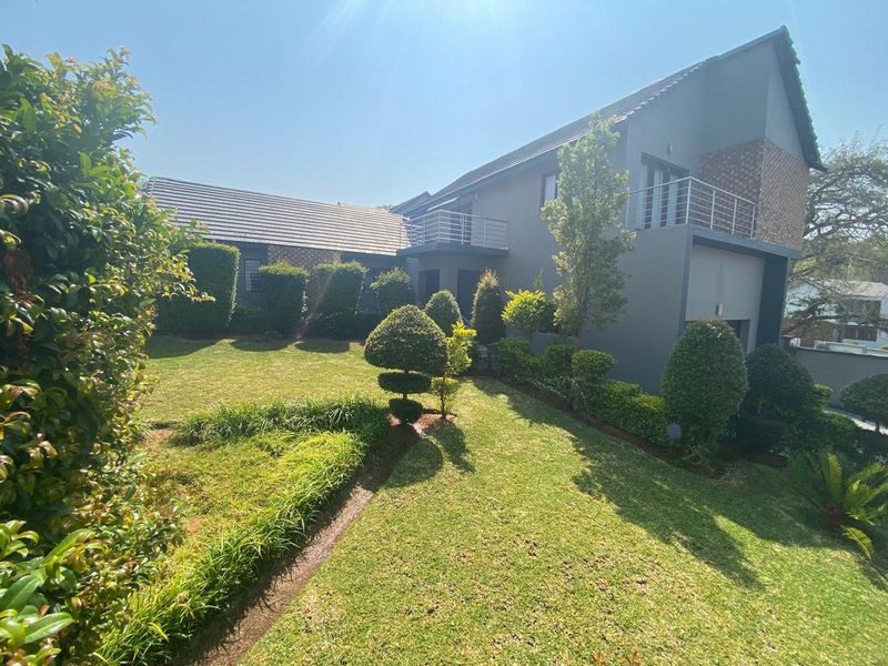 A well-maintained rear exterior view of the house featuring a landscaped garden, tiled roof, and an upper-level balcony with metal railings.