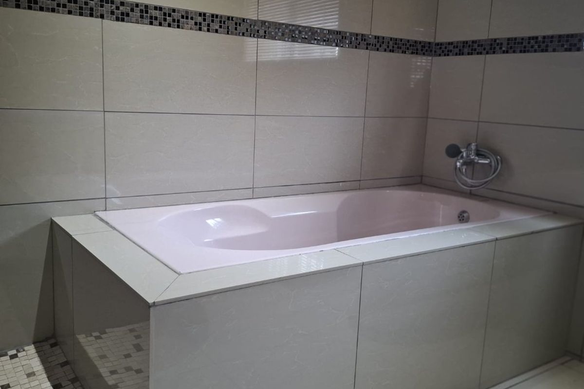 A bathroom featuring a built-in bathtub with light-colored ceramic wall tiles, a decorative mosaic border, and chrome fixtures.