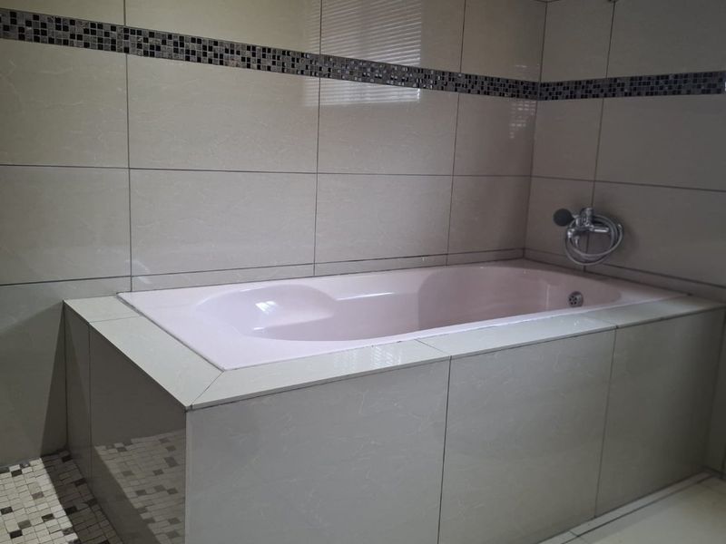 A bathroom featuring a built-in bathtub with light-colored ceramic wall tiles, a decorative mosaic border, and chrome fixtures.