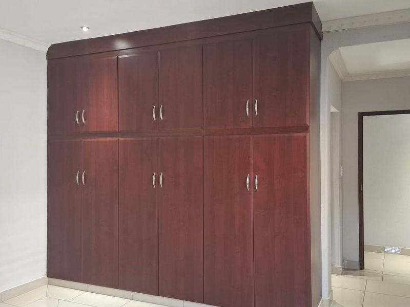 A clean, empty bedroom featuring dark wood built-in cupboards, tiled flooring, and modern recessed downlighting.