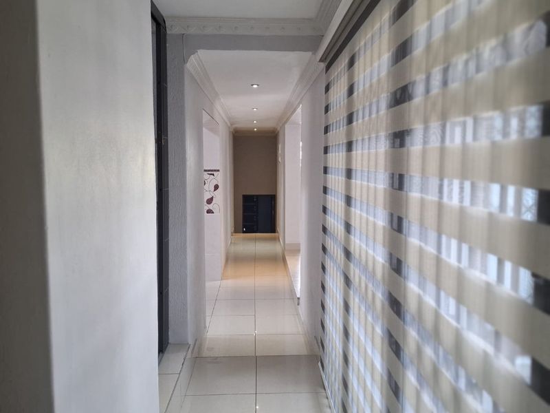 A bright, clean hallway featuring neutral tiled flooring, recessed ceiling lighting, and decorative cornice detailing.