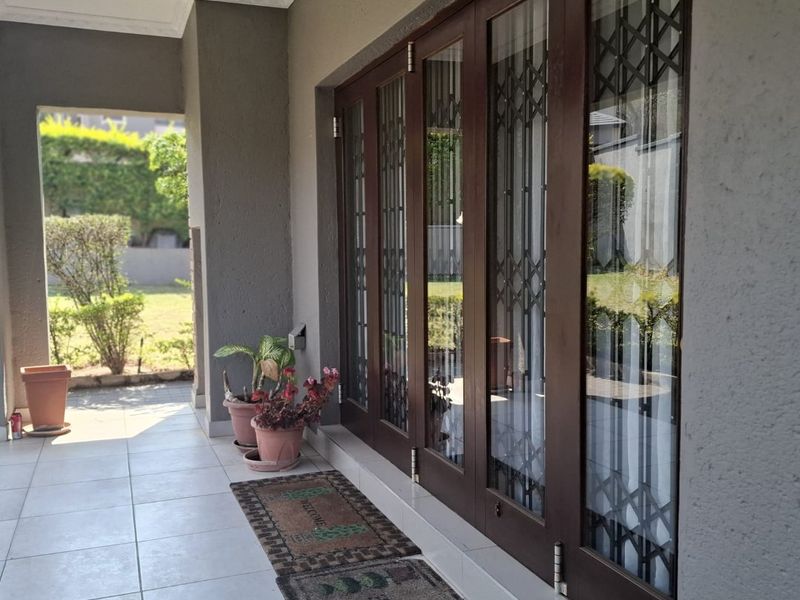 A covered patio area featuring tiled flooring, recessed downlights, and folding glass doors with integrated security gates, providing access to the garden.