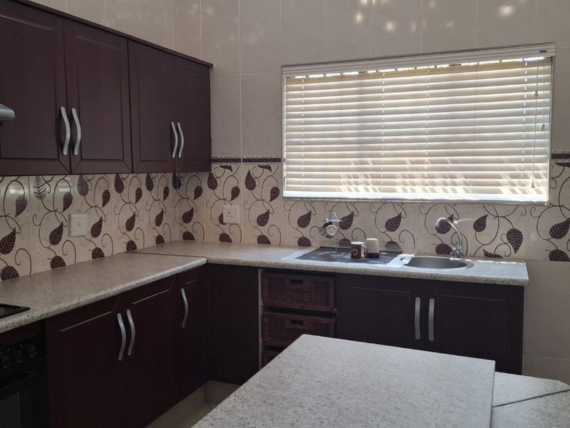 A functional kitchen featuring dark wood cabinetry, granite-look laminate countertops, tiled backsplash, and a built-in oven with a window providing natural light.