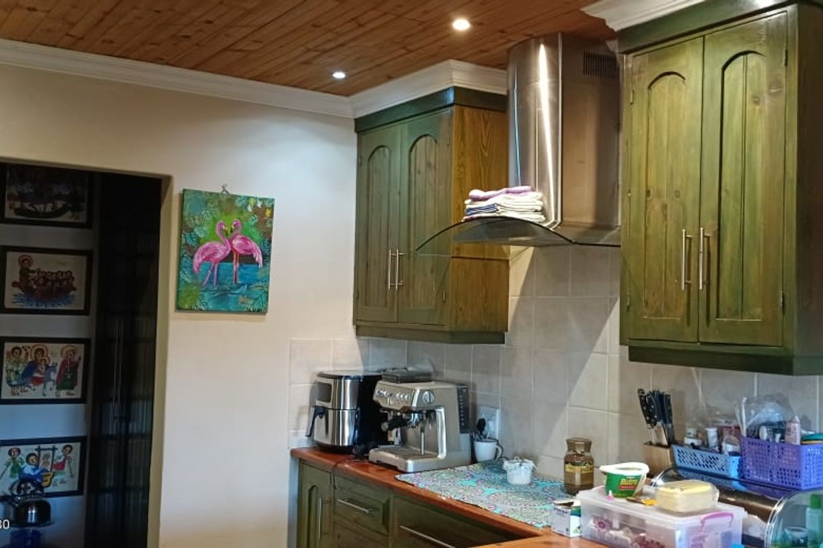 A kitchen area featuring green-toned wooden cabinetry, a stainless steel extractor fan, and tiled splashbacks with a timber-paneled ceiling.