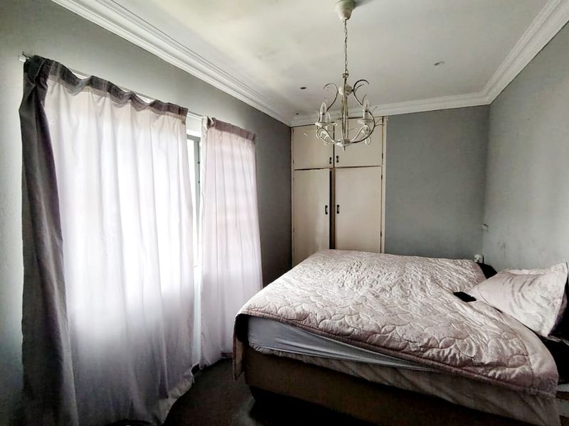 A bedroom featuring built-in cupboards, crown molding, and a central light fixture, offering a functional space with potential for cosmetic updates.