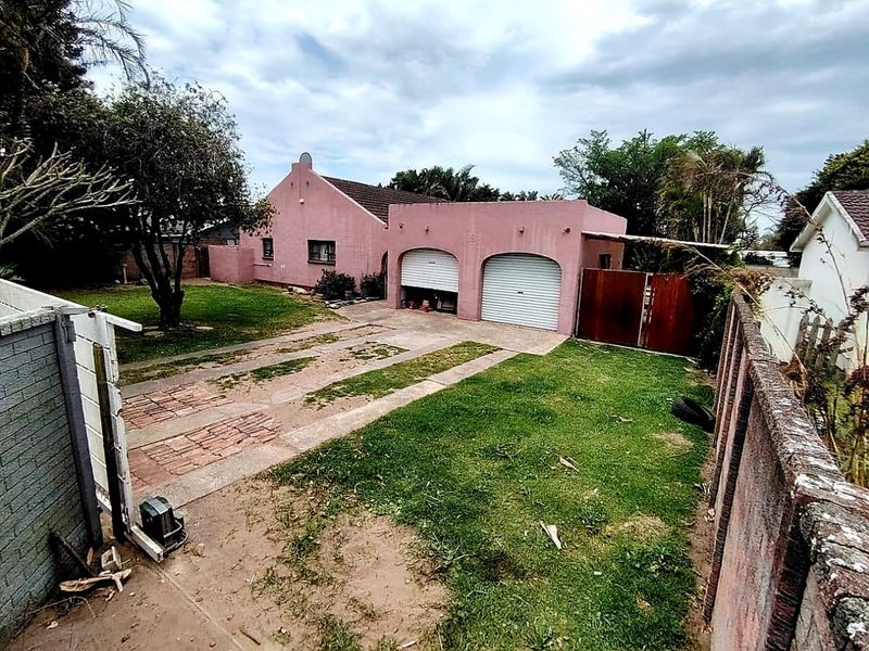 Front view of a single-story house featuring a double garage with roller shutter doors, a brick driveway, and a surrounding boundary wall.