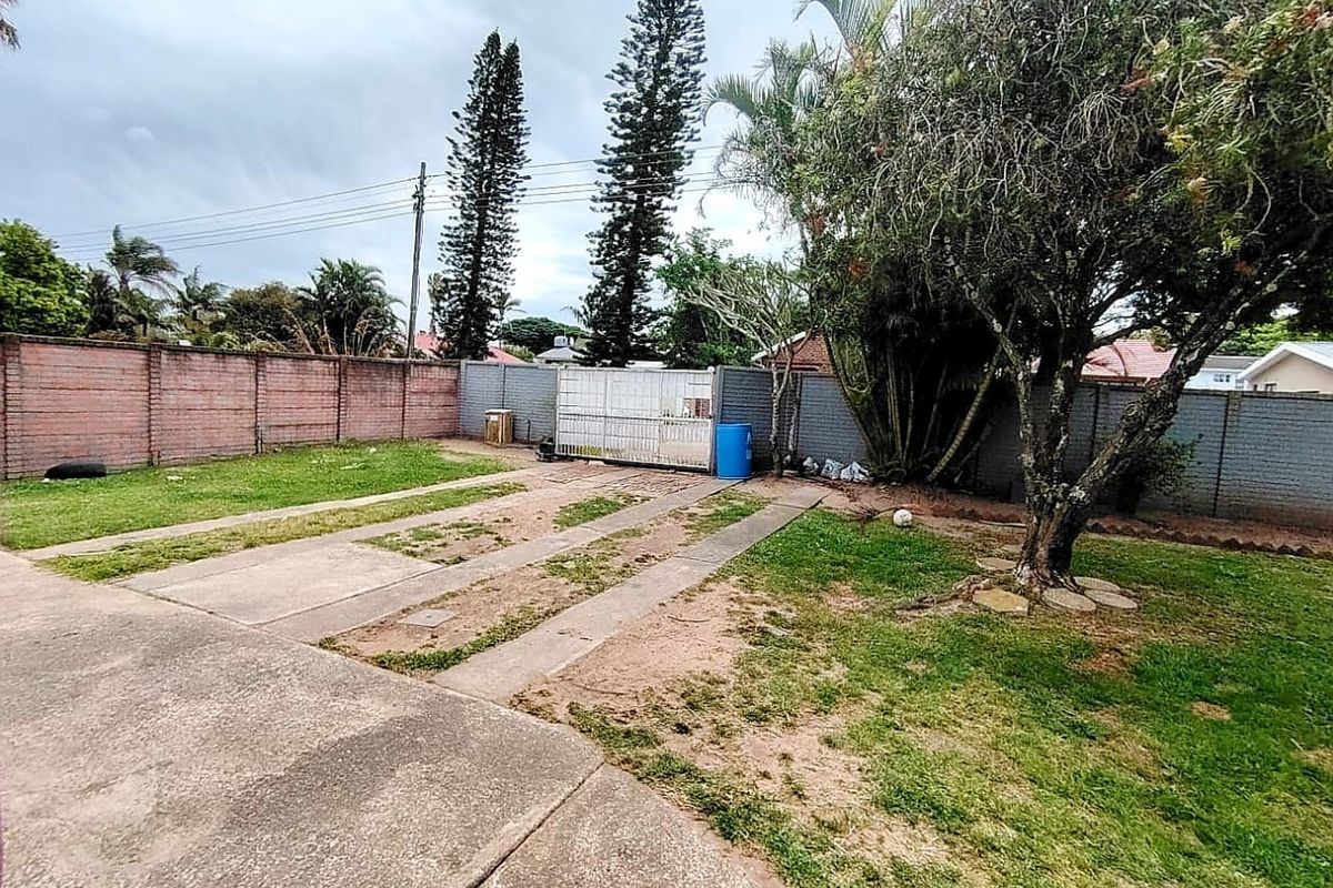 A spacious rear garden area featuring a concrete driveway, established trees, and secure brick boundary walls, offering potential for landscaping and outdoor improvement.