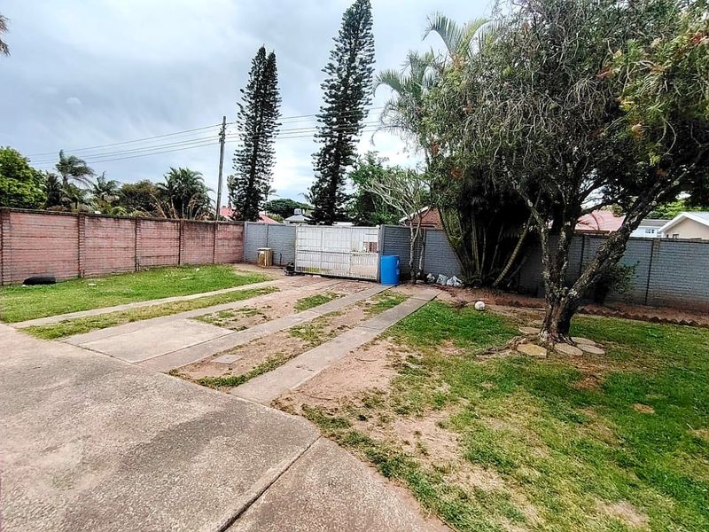 A spacious rear garden area featuring a concrete driveway, established trees, and secure brick boundary walls, offering potential for landscaping and outdoor improvement.
