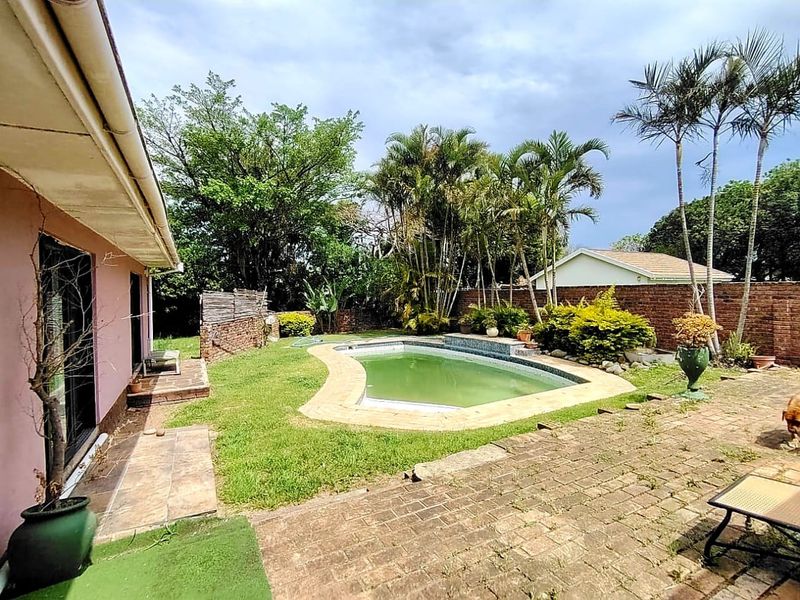 Outdoor pool area featuring a swimming pool, brick paving, and a perimeter boundary wall, set within a garden space.