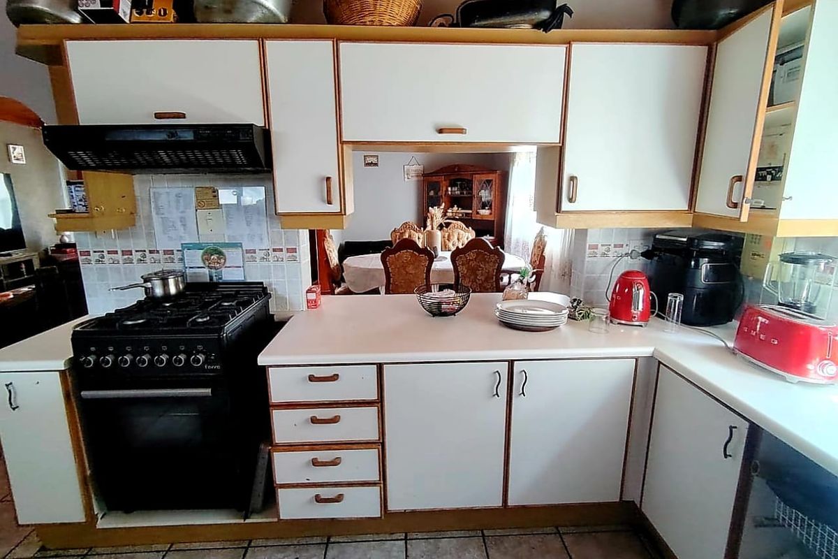 A functional kitchen featuring white laminate cabinetry, a gas stove with extractor fan, tiled backsplash, and tiled flooring with a pass-through to the dining area.