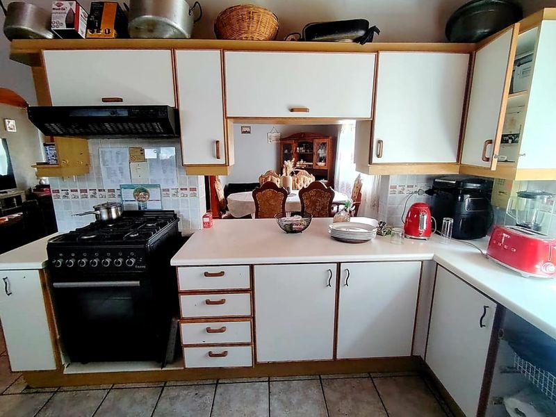 A functional kitchen featuring white laminate cabinetry, a gas stove with extractor fan, tiled backsplash, and tiled flooring with a pass-through to the dining area.