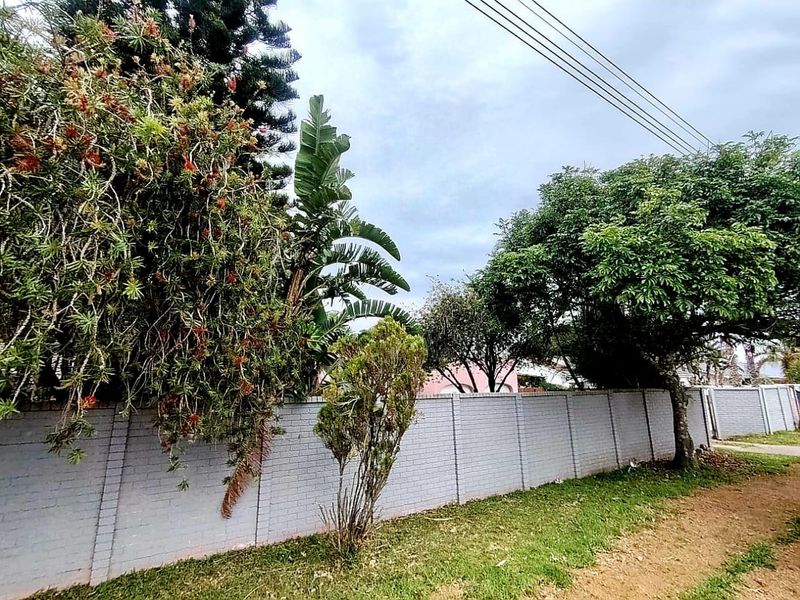 A street-level view of the property boundary featuring a solid brick wall and mature garden landscaping.