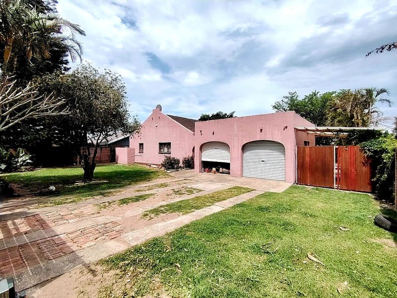 Front view of a residential property featuring a double garage with roller shutter doors, a brick driveway, and a spacious front lawn.