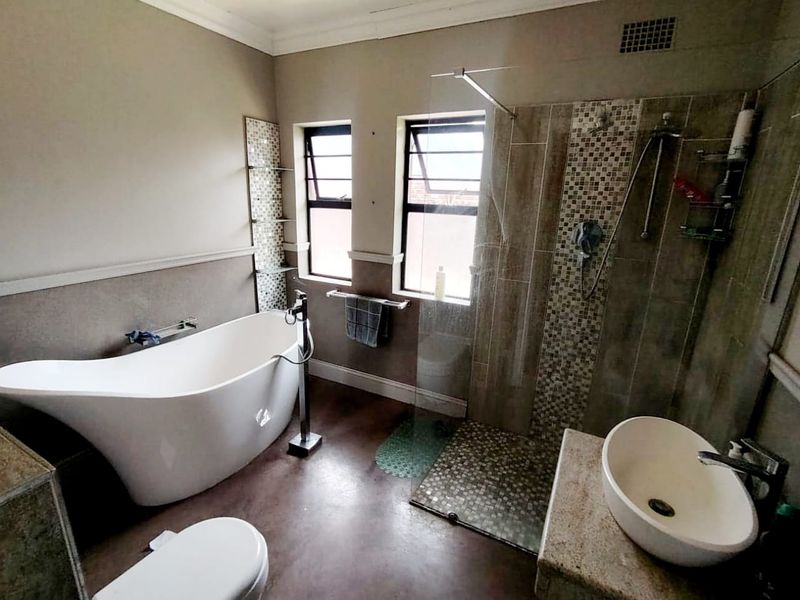 Modern bathroom featuring a freestanding bathtub, walk-in shower with glass screen, vessel sink on a stone vanity, and mosaic tile detailing.