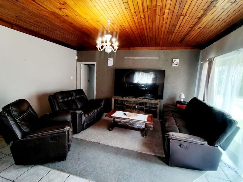 A living room featuring a distinctive timber-clad ceiling, tiled flooring, and a central chandelier, offering a cozy space for relaxation.