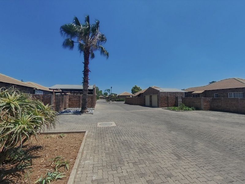 A view of the complex driveway featuring paved surfaces, brick boundary walls, and multiple townhouse units with tiled roofs.