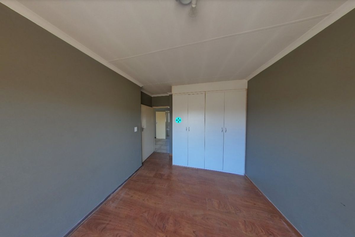 An empty bedroom featuring laminate flooring, neutral grey walls, and built-in cupboards, offering a clean and versatile space ready for personalization.