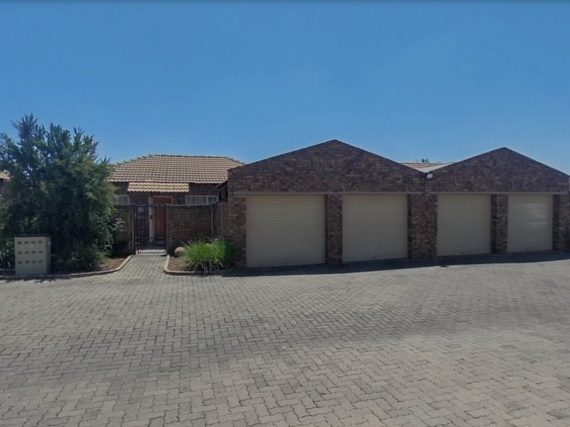 Front exterior view of a townhouse featuring a triple garage with roll-up doors, brick facade, tiled roof, and a paved driveway.