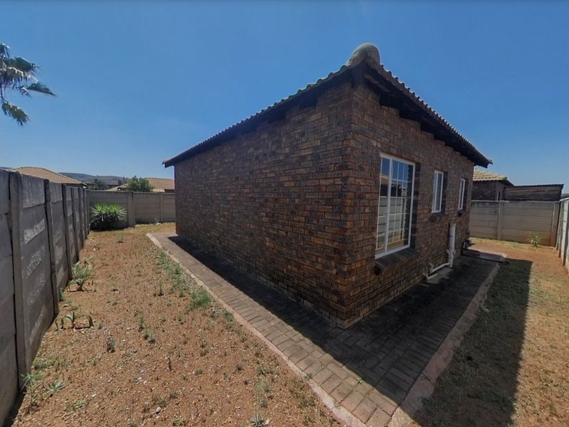 Rear view of the townhouse featuring a face brick exterior, tiled roof, and a paved walkway surrounding the building within a walled garden area.