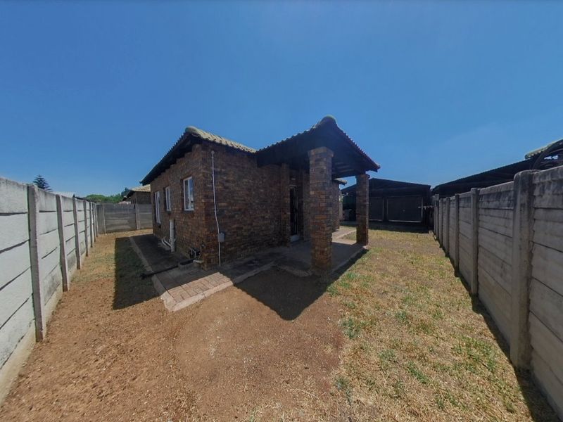 Rear view of a face brick townhouse featuring a covered patio, paved walkway, and enclosed garden area with precast concrete boundary walls.