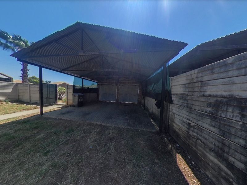 A covered carport area with a corrugated metal roof, paved flooring, and precast concrete boundary walls.