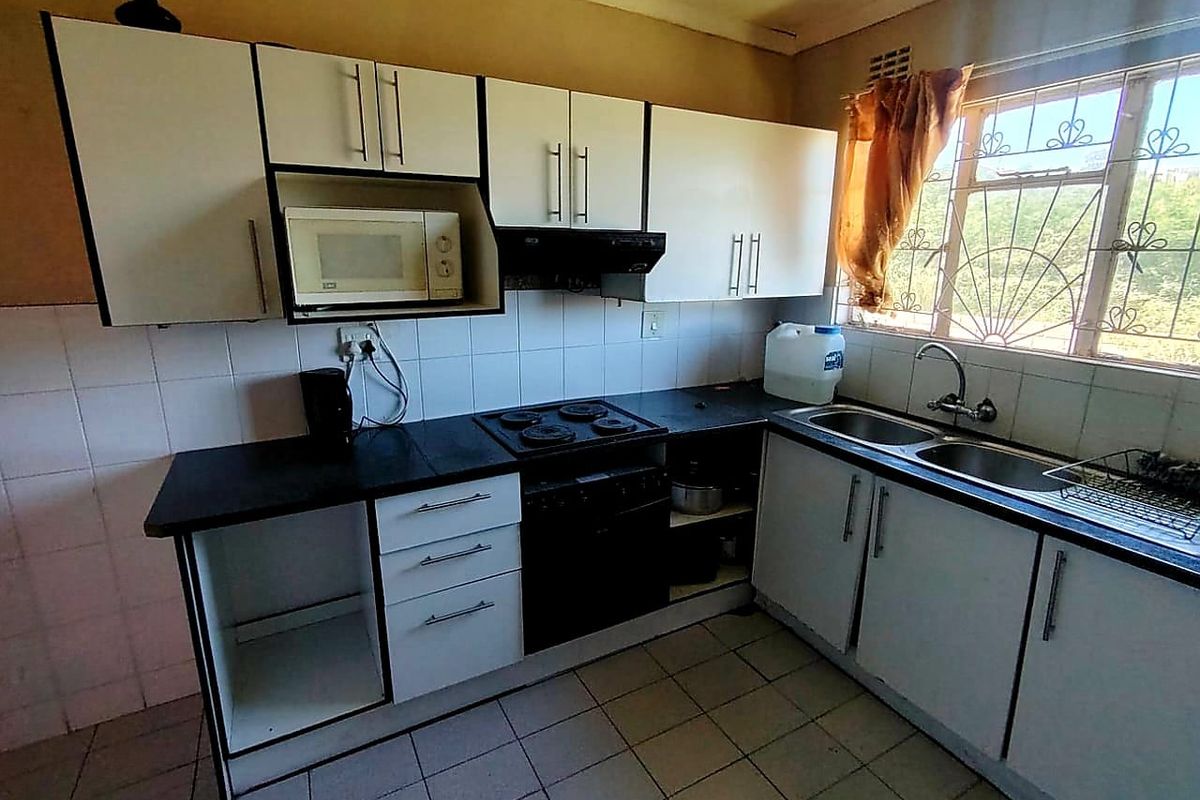 A functional kitchen featuring white cabinetry, dark countertops, an electric hob, and a double sink, with potential for cosmetic updates to modernize the space.