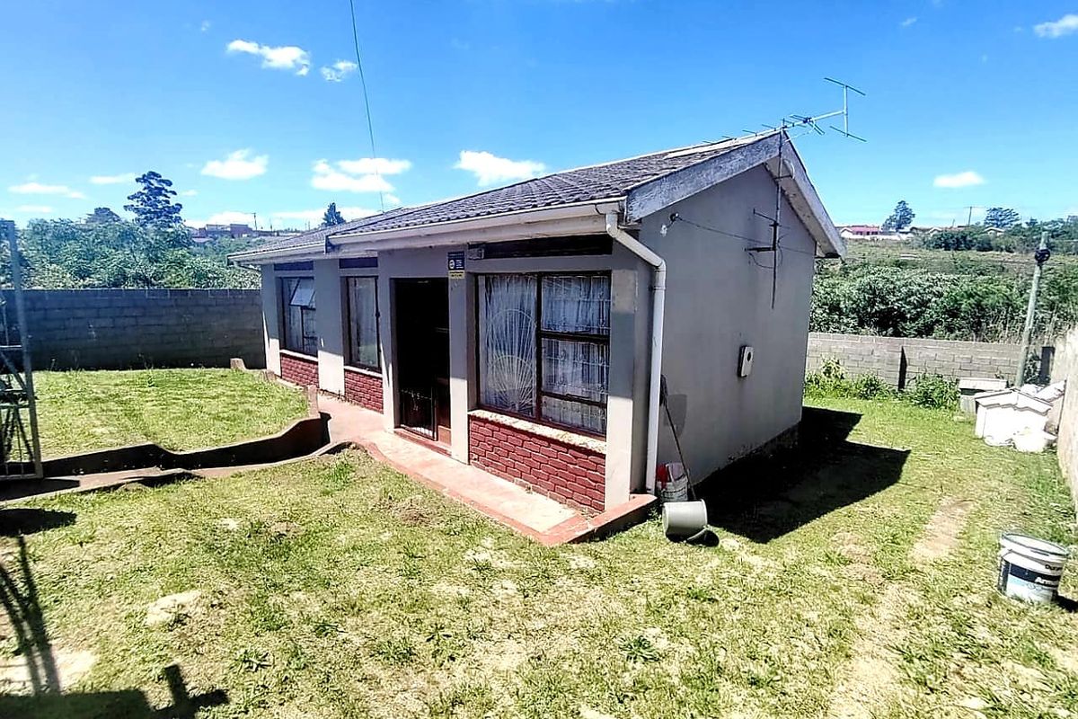 Rear view of a detached house featuring a tiled roof, brick and plaster facade, and a surrounding concrete boundary wall on a grassed plot.