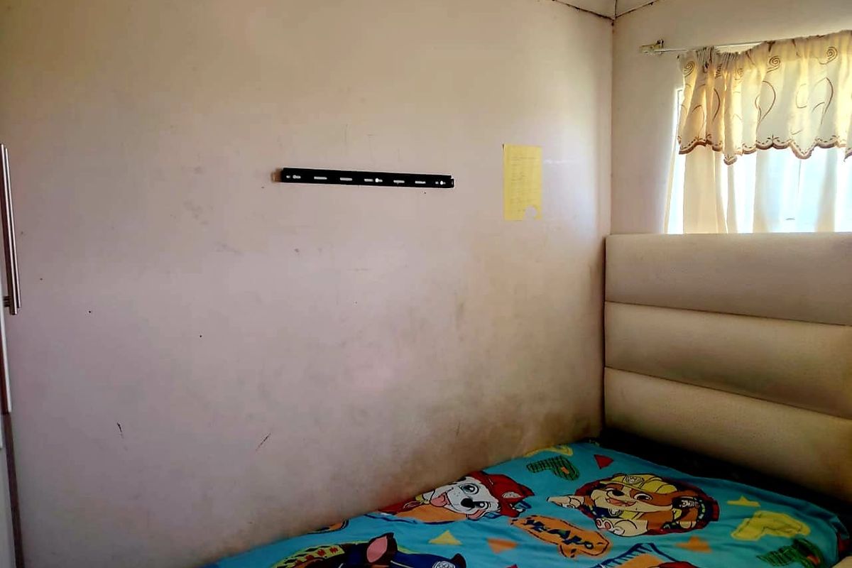 A compact bedroom featuring a built-in wardrobe and window, currently showing signs of wear on the wall surfaces.