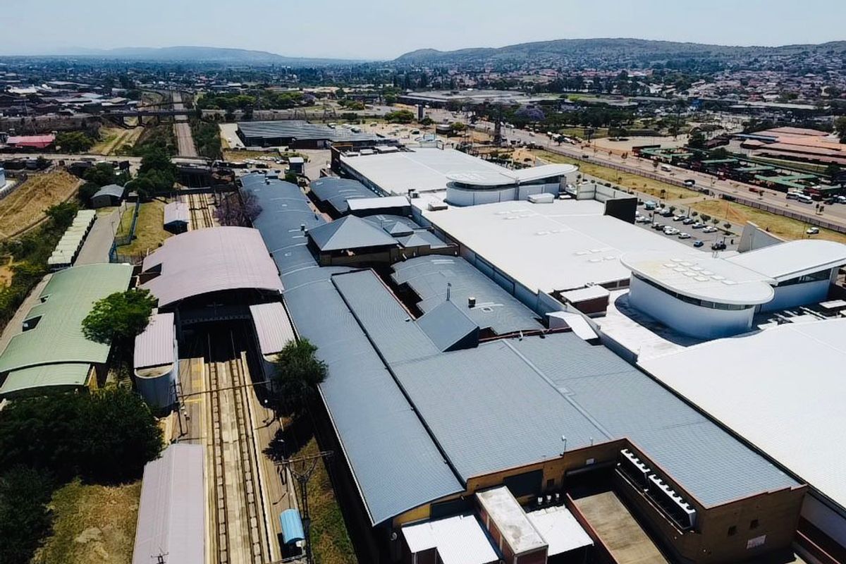 Aerial view of a large commercial complex featuring extensive metal roofing, integrated railway infrastructure, and surrounding urban landscape.