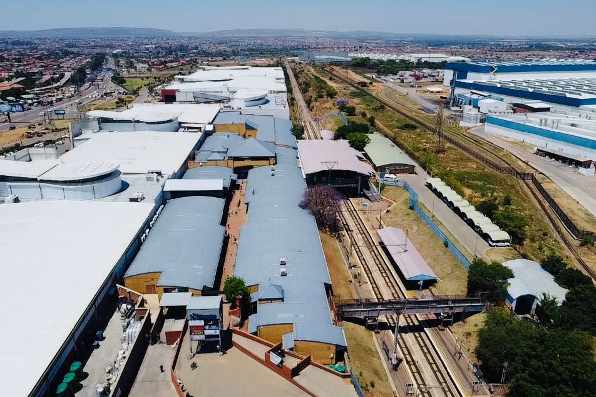 Aerial view of a large commercial industrial complex featuring extensive warehouse roofing, adjacent railway infrastructure, and surrounding urban landscape.