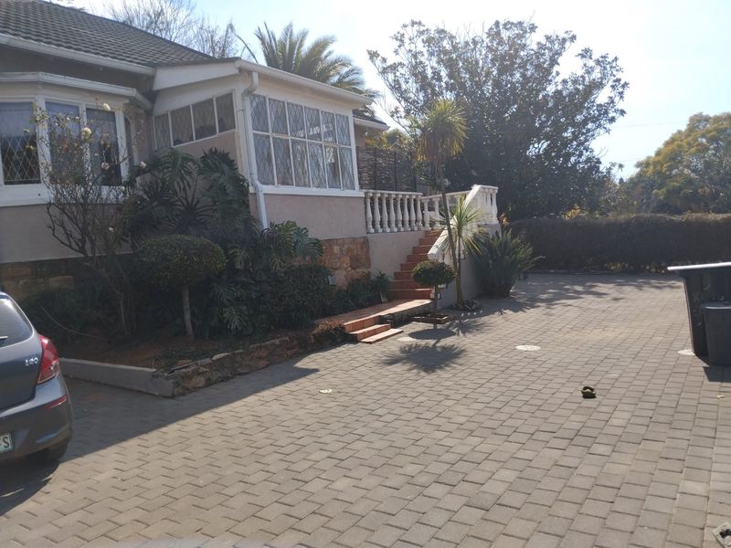 Front exterior view of the house featuring a paved driveway, stone retaining wall, and a staircase leading to an elevated entrance area.