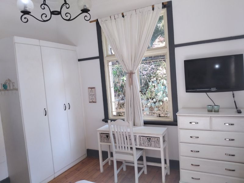 A bedroom featuring timber flooring, a built-in wardrobe, and a leaded glass window with dark-painted trim.