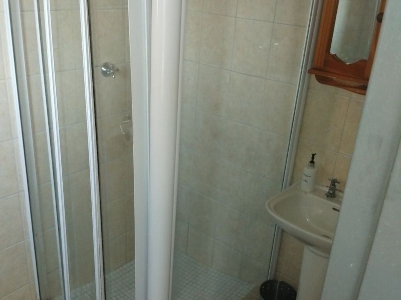 A compact bathroom featuring a corner shower enclosure with a glass door and a pedestal basin with tiled finishes.