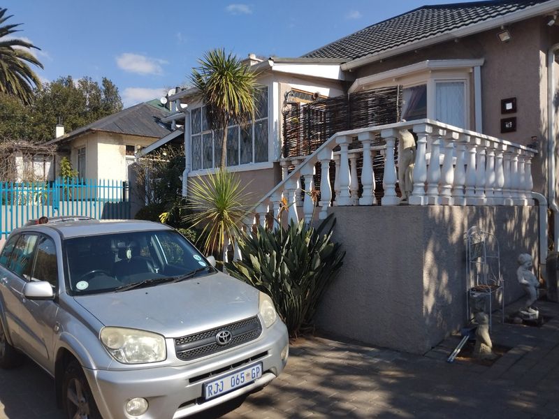 Front elevation of a residential house featuring a raised patio with a balustrade, bay window, and paved driveway area.